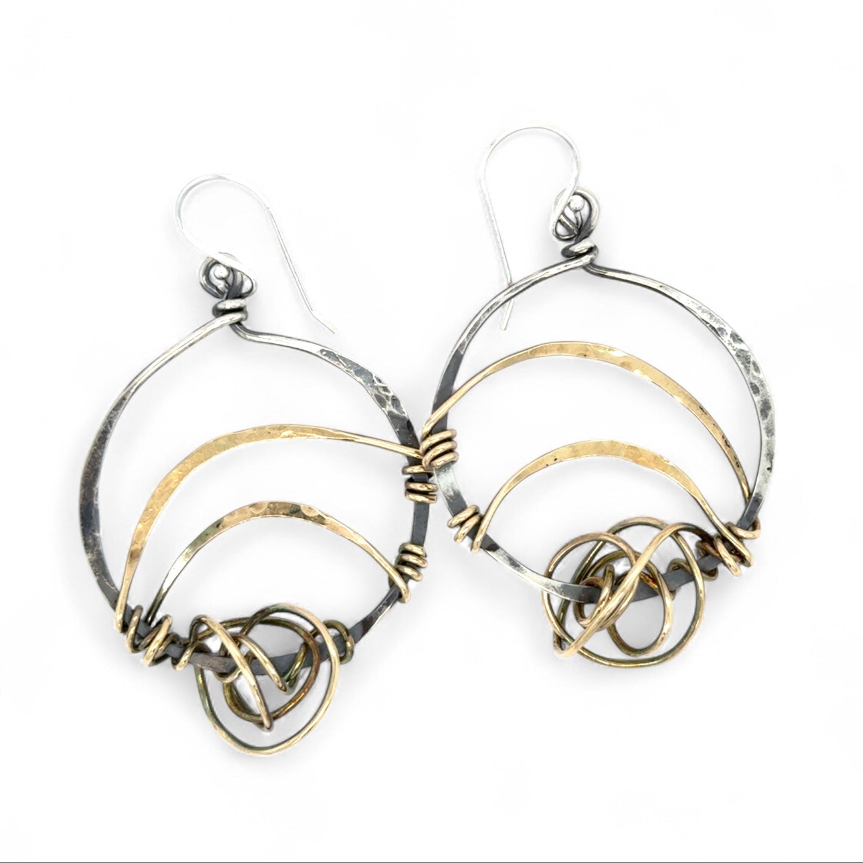 A pair of earrings featuring gestural knots of hand-formed hammered brass on oxidized sterling silver hoops