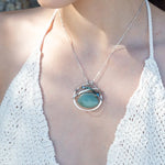 A sterling silver necklace with a moss-colored jade fan gemstone pendant featuring hammered bronze, oxidized sterling silver twist wire, and micro faceted ombre blue tourmaline gemstones, crystal, and pyrite.