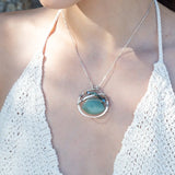 A sterling silver necklace with a moss-colored jade fan gemstone pendant featuring hammered bronze, oxidized sterling silver twist wire, and micro faceted ombre blue tourmaline gemstones, crystal, and pyrite.