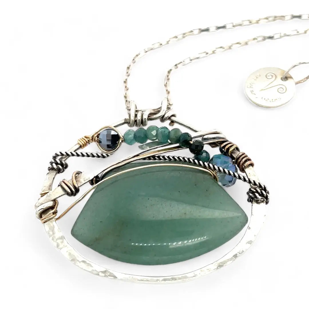 A sterling silver necklace with a moss-colored jade fan gemstone pendant featuring hammered bronze, oxidized sterling silver twist wire, and micro faceted ombre blue tourmaline gemstones, crystal, and pyrite.