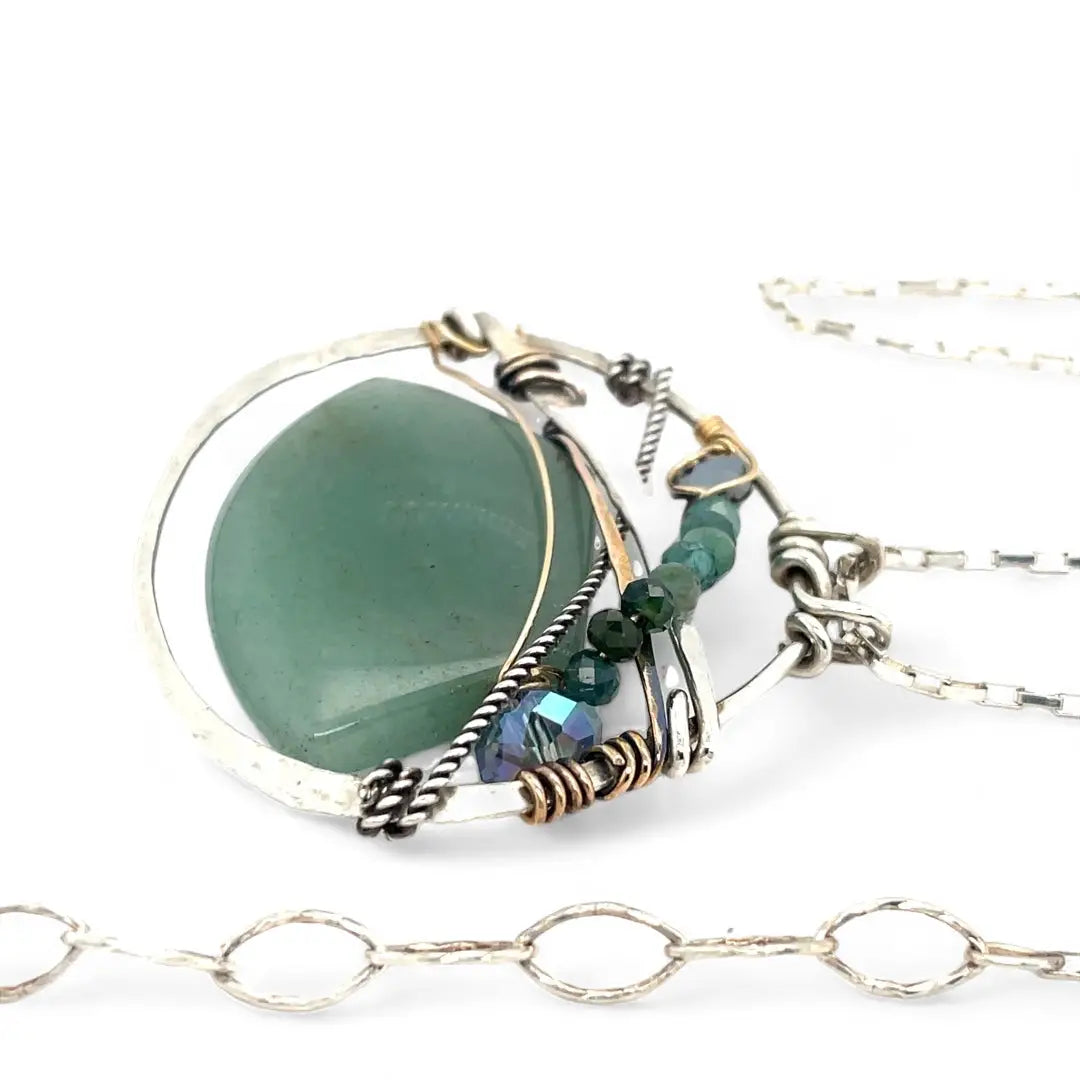 A sterling silver necklace with a moss-colored jade fan gemstone pendant featuring hammered bronze, oxidized sterling silver twist wire, and micro faceted ombre blue tourmaline gemstones, crystal, and pyrite.