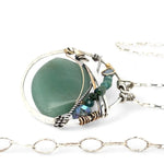 A sterling silver necklace with a moss-colored jade fan gemstone pendant featuring hammered bronze, oxidized sterling silver twist wire, and micro faceted ombre blue tourmaline gemstones, crystal, and pyrite.
