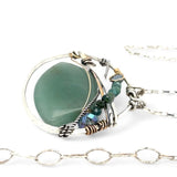 A sterling silver necklace with a moss-colored jade fan gemstone pendant featuring hammered bronze, oxidized sterling silver twist wire, and micro faceted ombre blue tourmaline gemstones, crystal, and pyrite.