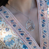 A sterling silver nautilus shell necklace with micro-faceted aquamarine and crystal beads along bronze lines, culminating in a faceted rose quartz gemstone center.