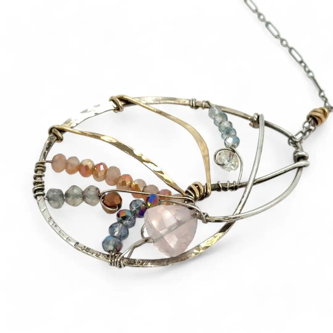 A sterling silver nautilus shell necklace with micro-faceted aquamarine and crystal beads along bronze lines, culminating in a faceted rose quartz gemstone center.