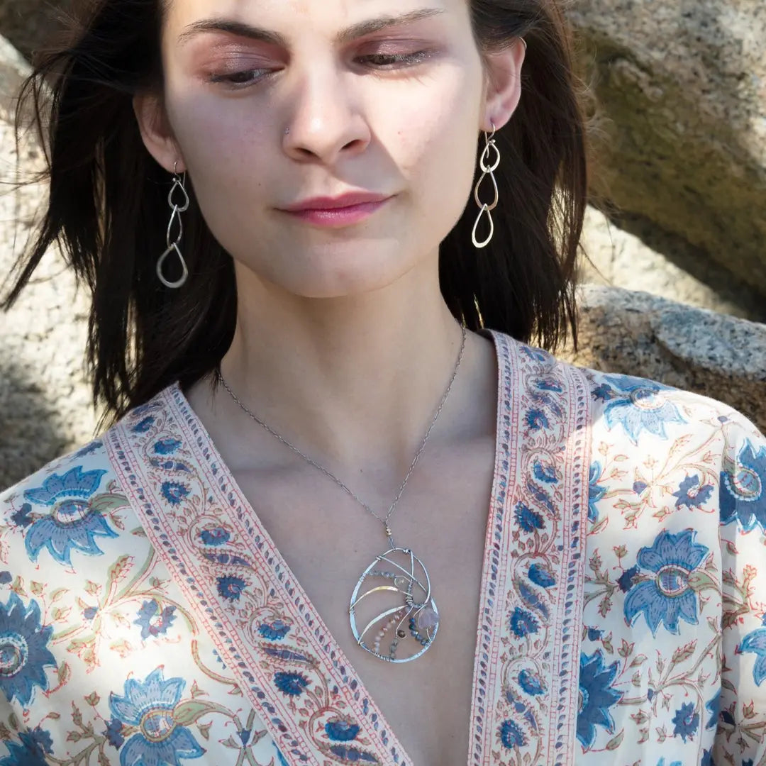 A sterling silver nautilus shell necklace with micro-faceted aquamarine and crystal beads along bronze lines, culminating in a faceted rose quartz gemstone center.