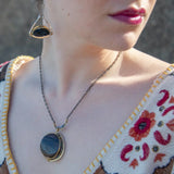 A necklace with a smooth brown jasper round gemstone, surrounded by faceted pyrite, set in hand-formed brass, with an adjustable darkened chain and sterling silver clasp.