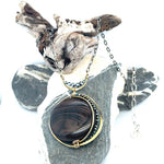 A necklace with a smooth brown jasper round gemstone, surrounded by faceted pyrite, set in hand-formed brass, with an adjustable darkened chain and sterling silver clasp.