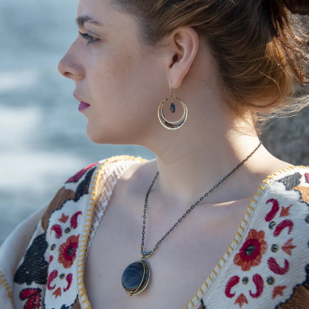 A necklace with a smooth brown jasper round gemstone, surrounded by faceted pyrite, set in hand-formed brass, with an adjustable darkened chain and sterling silver clasp.