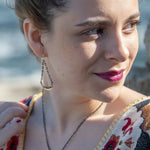 A pair of earrings featuring hand-formed brass arches with faceted pyrite gemstones, suspended from black chain links with sterling silver French hooks.