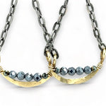 A pair of earrings featuring hand-formed brass arches with faceted pyrite gemstones, suspended from black chain links with sterling silver French hooks.
