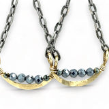 A pair of earrings featuring hand-formed brass arches with faceted pyrite gemstones, suspended from black chain links with sterling silver French hooks.