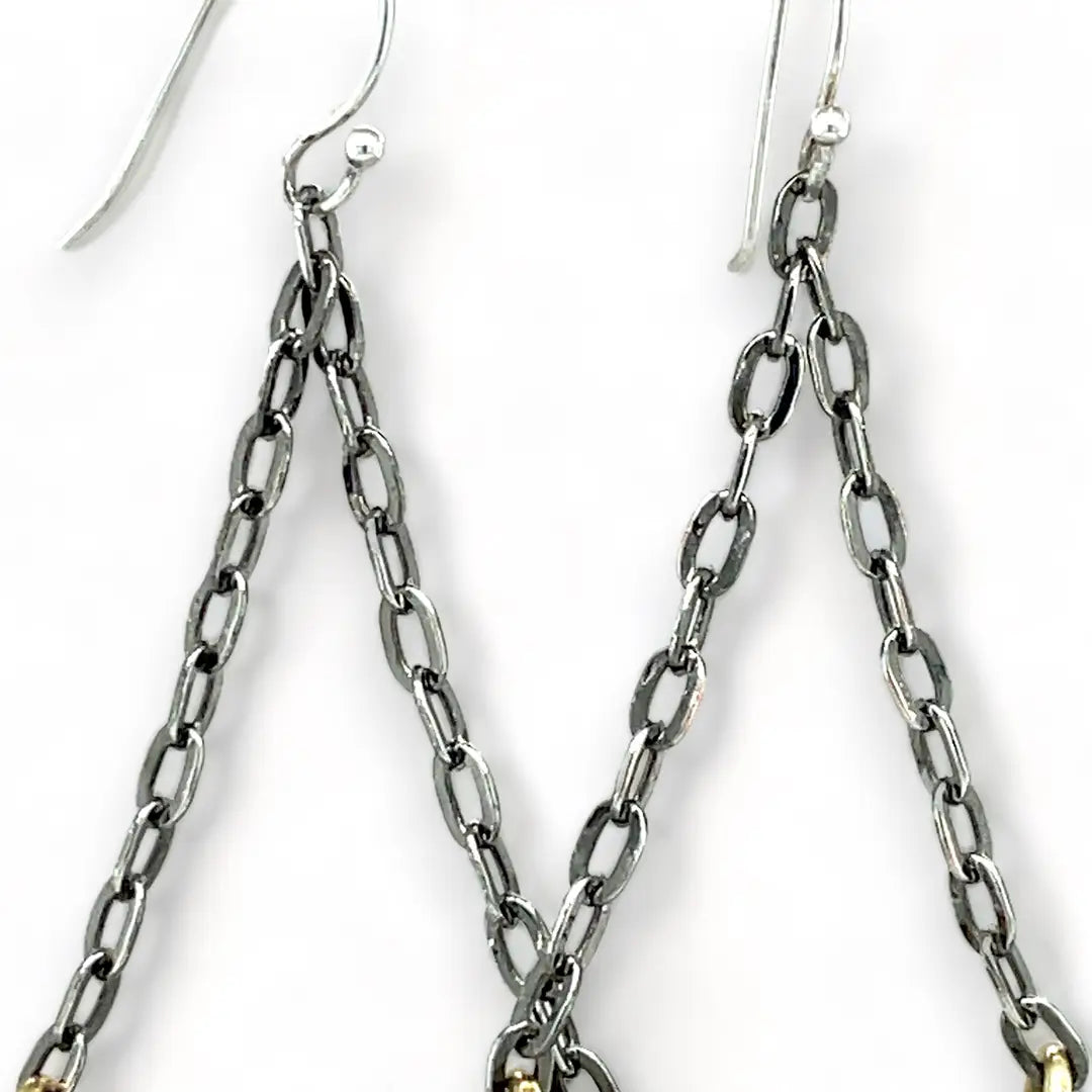 A pair of earrings featuring hand-formed brass arches with faceted pyrite gemstones, suspended from black chain links with sterling silver French hooks.