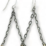 A pair of earrings featuring hand-formed brass arches with faceted pyrite gemstones, suspended from black chain links with sterling silver French hooks.