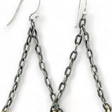 A pair of earrings featuring hand-formed brass arches with faceted pyrite gemstones, suspended from black chain links with sterling silver French hooks.