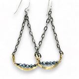 A pair of earrings featuring hand-formed brass arches with faceted pyrite gemstones, suspended from black chain links with sterling silver French hooks.