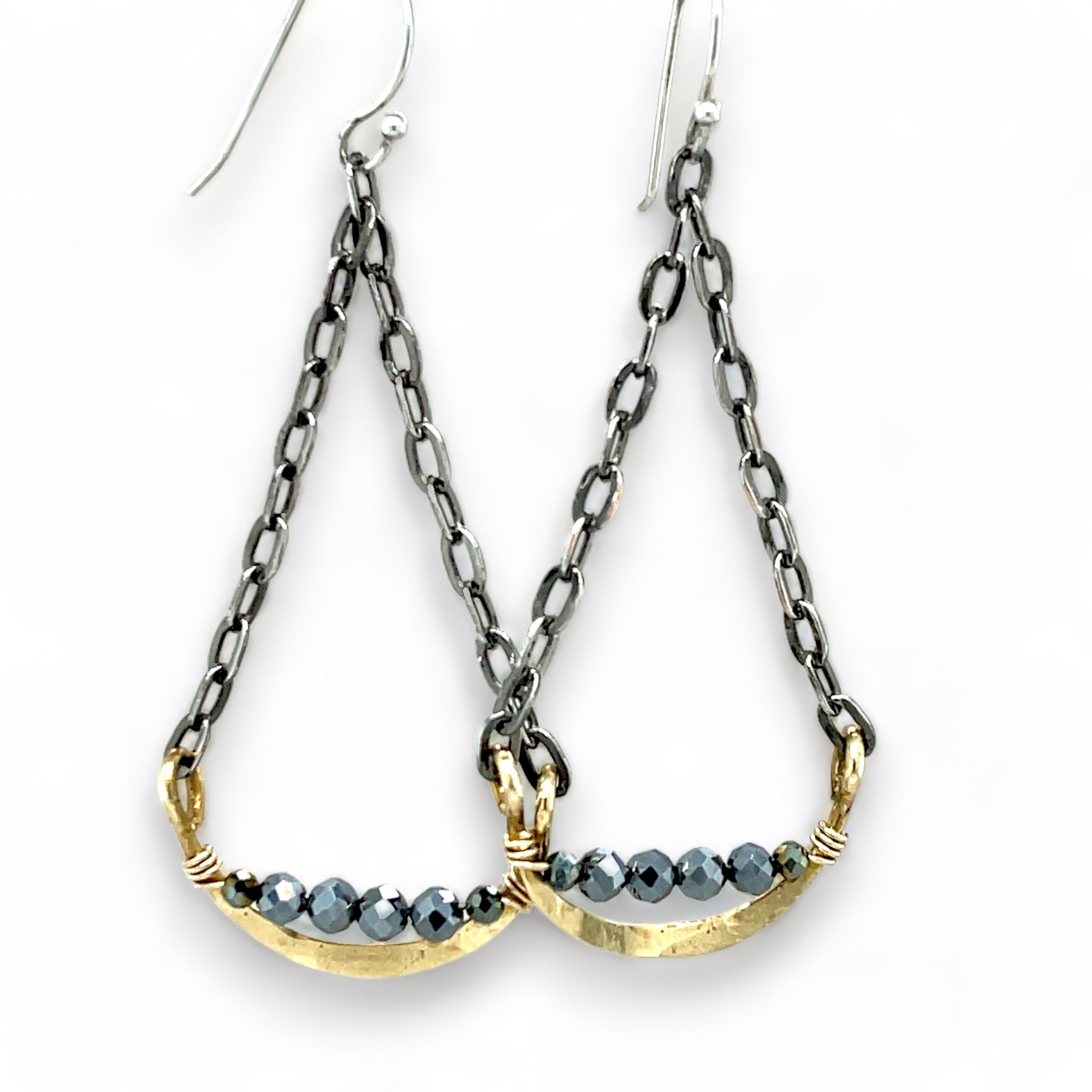 A pair of earrings featuring hand-formed brass arches with faceted pyrite gemstones, suspended from black chain links with sterling silver French hooks.