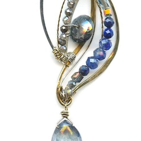 Sterling silver and brass wing shapes combined to make one pendant featuring moonstone, blue crystal, labradorite, kyanite, and lapis gemstones with a blue quartz hanging drop to complete the necklace