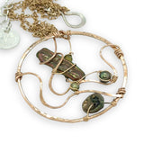 A collection of olive green fresh water pearls are woven in layers of gold filled hammered wire onto a handmade circle gold pendant necklace