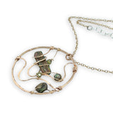 A collection of olive green fresh water pearls are woven in layers of gold filled hammered wire onto a handmade circle gold pendant necklace