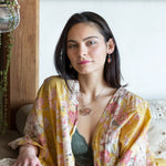 A darkened sterling silver pallete pendant necklace with bronze hammered swirls, featuring a series of faceted gemstones including amethyst and rhodocrosite, peach fresh water coin pearl, and crystal, complemented by a rose gold chain and a silver textured chain.