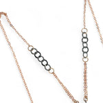 A darkened sterling silver pallete pendant necklace with bronze hammered swirls, featuring a series of faceted gemstones including amethyst and rhodocrosite, peach fresh water coin pearl, and crystal, complemented by a rose gold chain and a silver textured chain.