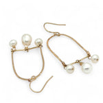 A pair of brass hammered open archway earrings with freshwater pearls attached to them