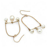 A pair of brass hammered open archway earrings with freshwater pearls attached to them