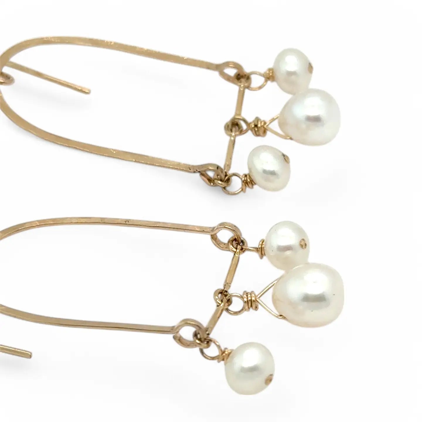 A pair of brass hammered open archway earrings with freshwater pearls attached to them