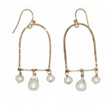 A pair of brass hammered open archway earrings with freshwater pearls attached to them