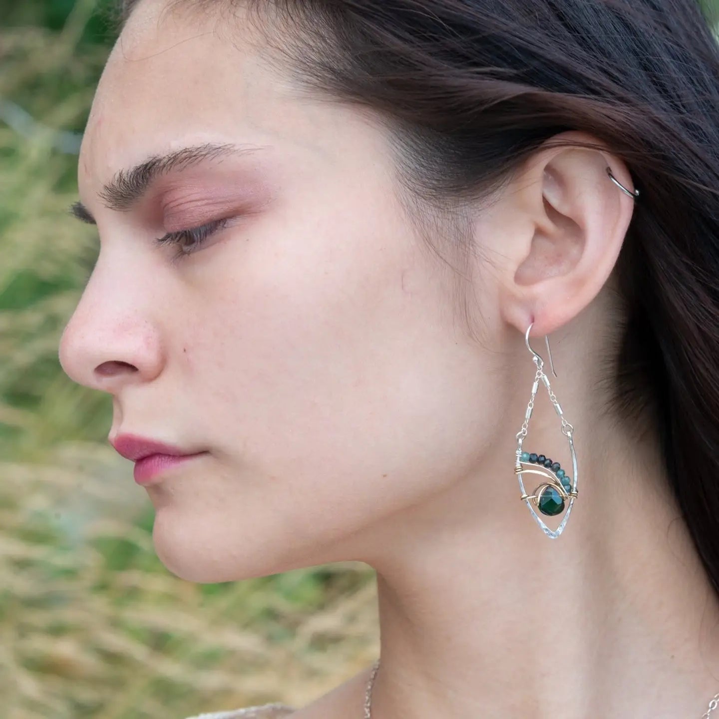 A pair of sterling silver leaf earrings with faceted green amethyst and blue tourmaline gemstones, wrapped in hand-formed hammered brass with sterling silver tube chain tops