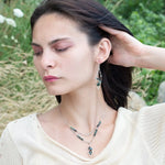 A pair of sterling silver leaf earrings with faceted green amethyst and blue tourmaline gemstones, wrapped in hand-formed hammered brass with sterling silver tube chain tops