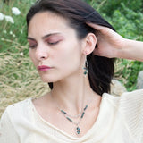 A pair of sterling silver leaf earrings with faceted green amethyst and blue tourmaline gemstones, wrapped in hand-formed hammered brass with sterling silver tube chain tops