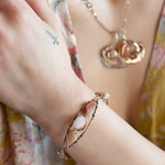 An oxidized sterling silver cuff bracelet with gold-filled wraps, featuring pink opal gemstones and rhodochrosite on a hammered bronze structure