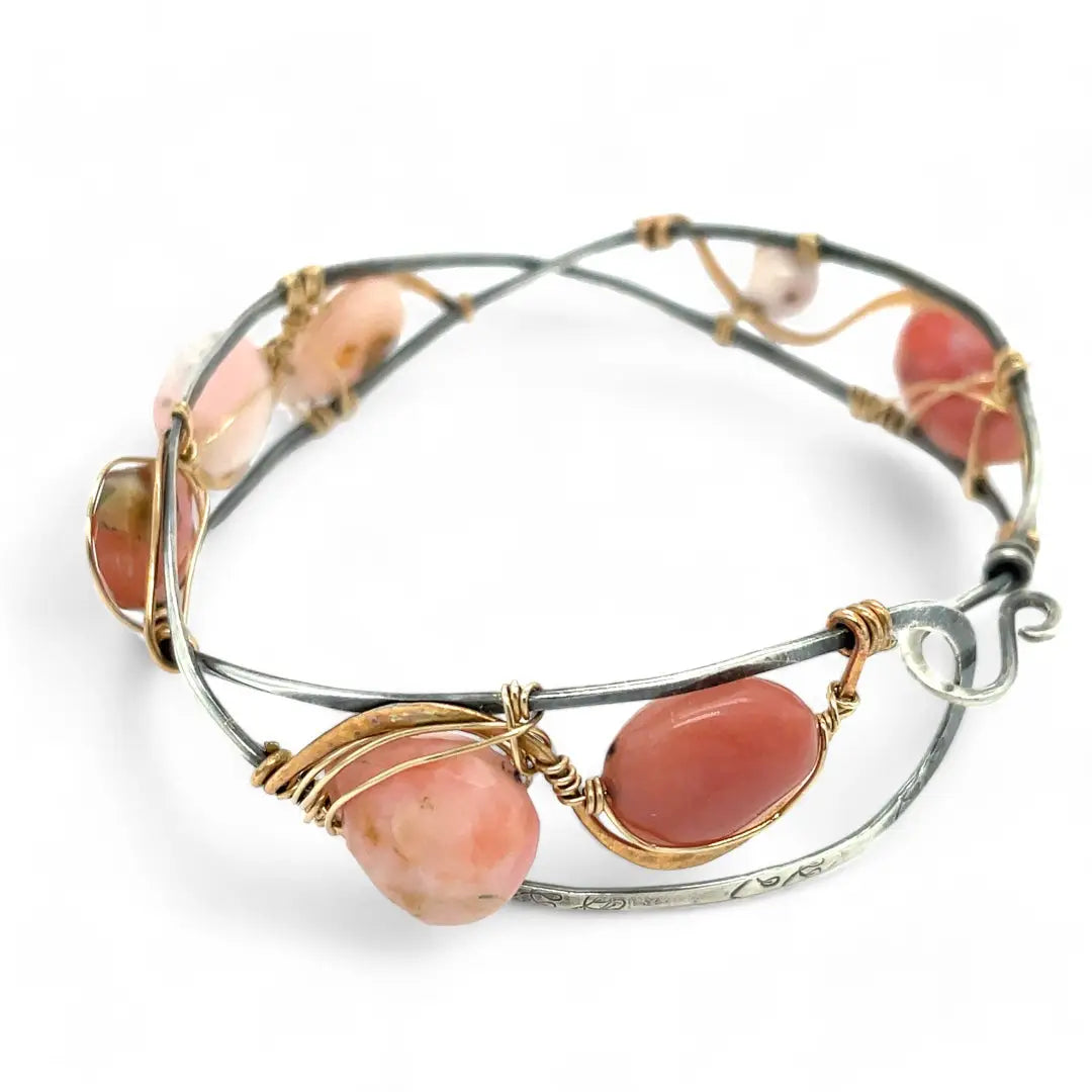 An oxidized sterling silver cuff bracelet with gold-filled wraps, featuring pink opal gemstones and rhodochrosite on a hammered bronze structure