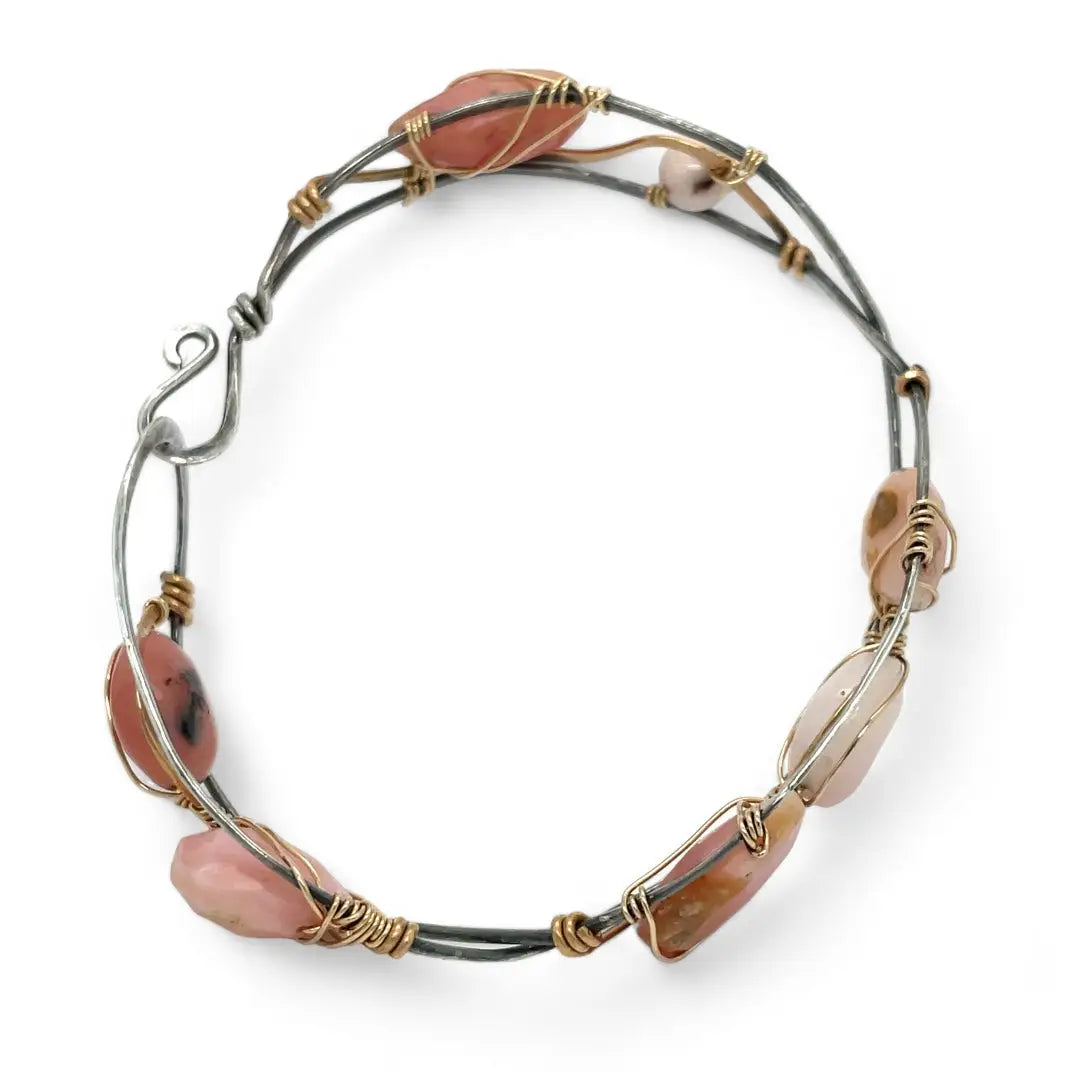 An oxidized sterling silver cuff bracelet with gold-filled wraps, featuring pink opal gemstones and rhodochrosite on a hammered bronze structure