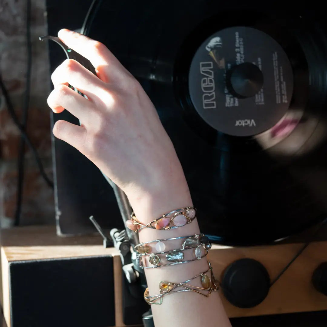 An oxidized sterling silver cuff bracelet with gold-filled wraps, featuring pink opal gemstones and rhodochrosite on a hammered bronze structure
