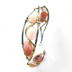 An oxidized sterling silver cuff bracelet with gold-filled wraps, featuring pink opal gemstones and rhodochrosite on a hammered bronze structure