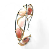 An oxidized sterling silver cuff bracelet with gold-filled wraps, featuring pink opal gemstones and rhodochrosite on a hammered bronze structure