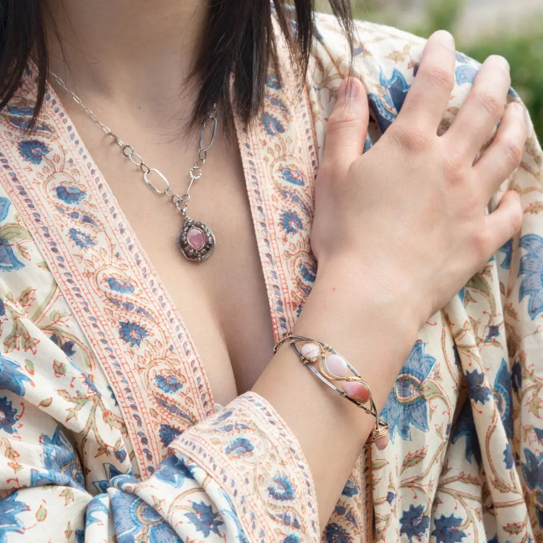 An oxidized sterling silver cuff bracelet with gold-filled wraps, featuring pink opal gemstones and rhodochrosite on a hammered bronze structure