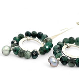 Handmade hammered sterling silver rings are outlined with faceted emerald gemstones hanging from a sterling silver hammered and twisted bar, accented with a silver fresh water pearl dangle