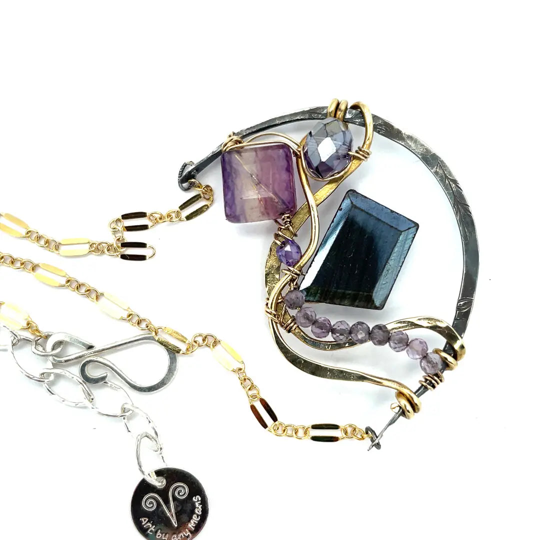 Dark labradorite parallelogram, banded fluorite, purple crystal, and amethyst gemstones ride waves of hammered brass inside a floral stamped and hammered oxidized sterling silver arch pendant on gold filled chain necklace