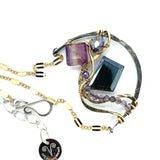 Dark labradorite parallelogram, banded fluorite, purple crystal, and amethyst gemstones ride waves of hammered brass inside a floral stamped and hammered oxidized sterling silver arch pendant on gold filled chain necklace
