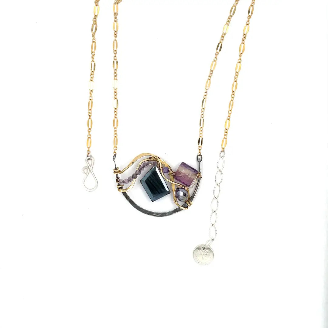 Dark labradorite parallelogram, banded fluorite, purple crystal, and amethyst gemstones ride waves of hammered brass inside a floral stamped and hammered oxidized sterling silver arch pendant on gold filled chain necklace