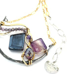 Dark labradorite parallelogram, banded fluorite, purple crystal, and amethyst gemstones ride waves of hammered brass inside a floral stamped and hammered oxidized sterling silver arch pendant on gold filled chain necklace