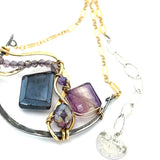 Dark labradorite parallelogram, banded fluorite, purple crystal, and amethyst gemstones ride waves of hammered brass inside a floral stamped and hammered oxidized sterling silver arch pendant on gold filled chain necklace