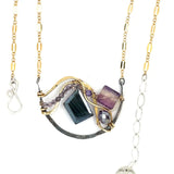 Dark labradorite parallelogram, banded fluorite, purple crystal, and amethyst gemstones ride waves of hammered brass inside a floral stamped and hammered oxidized sterling silver arch pendant on gold filled chain necklace