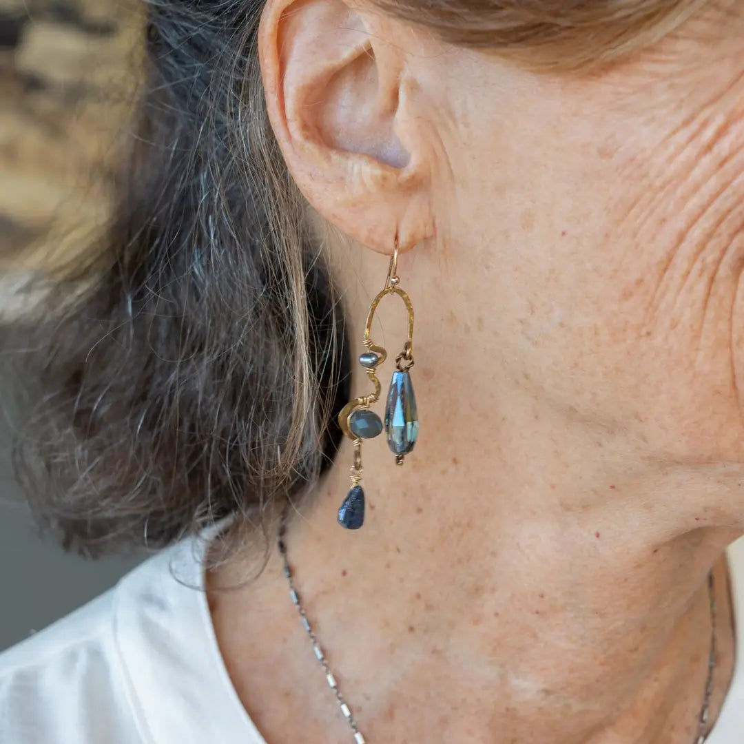 A pair of brass sculptural squiggle earrings with raw kyanite gemstone drops, an assortment of sparkly crystals, and fresh water pearls, featuring gold-filled French hooks.