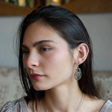 A pair of Prehnite smooth oval earrings with cool inclusions, adorned with hammered bronze, twisted oxidized sterling silver, and micro faceted watermelon tourmaline gemstones, attached to sterling silver French hooks.