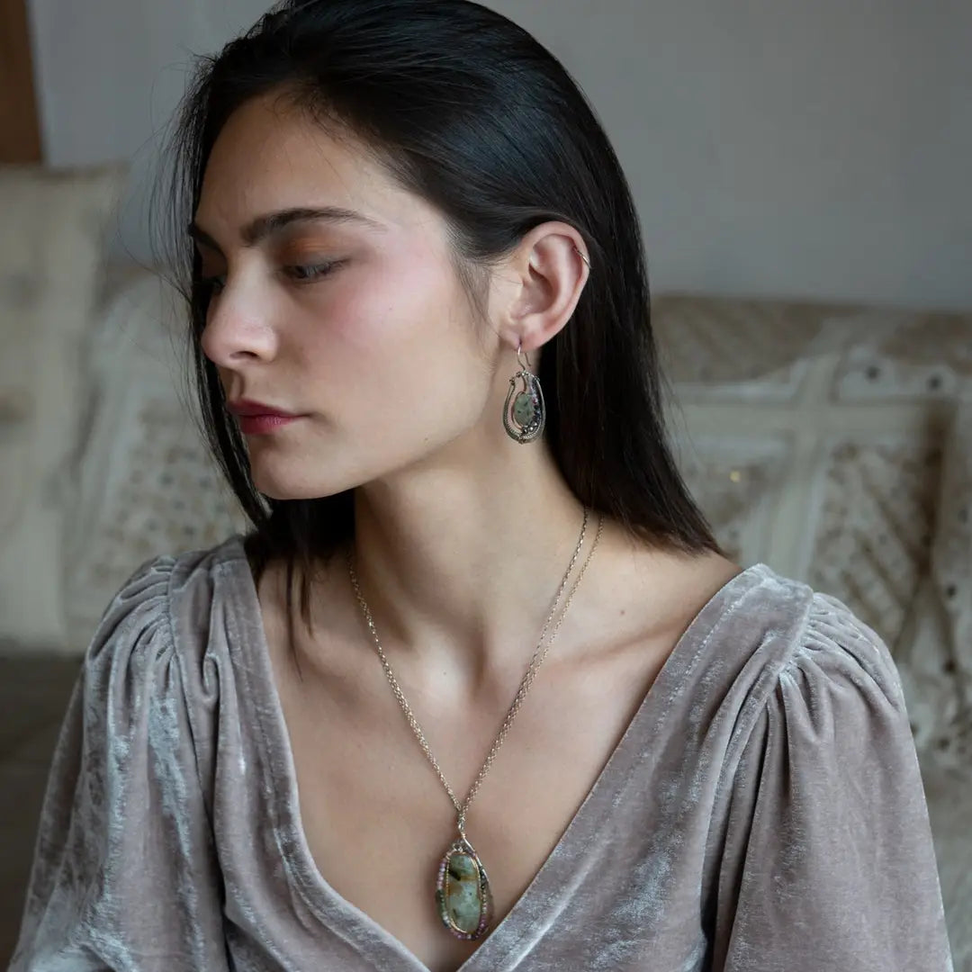 A pair of Prehnite smooth oval earrings with cool inclusions, adorned with hammered bronze, twisted oxidized sterling silver, and micro faceted watermelon tourmaline gemstones, attached to sterling silver French hooks.